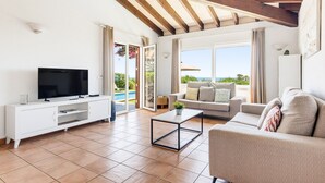 A living room with a TV, sofa, coffee table, and a view of the outdoors.