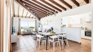 A spacious living area with a dining table, chairs, a sofa, and a view of the outdoors.