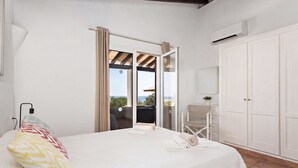 A bedroom with a bed, a chair, a wardrobe, and an air conditioning unit.