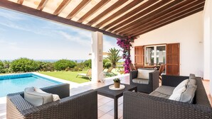 A covered outdoor seating area with wicker furniture, a pool, and a view of the landscape.