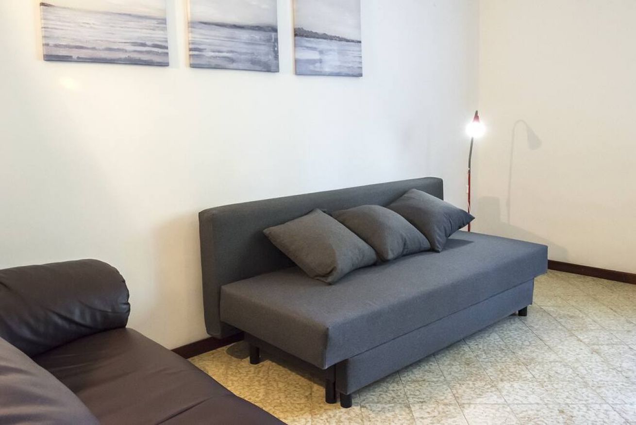 A grey sofa with cushions, a floor lamp, and three abstract paintings on the wall.