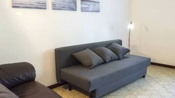 A grey sofa with cushions, a floor lamp, and three abstract paintings on the wall.