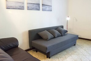 Un sofá gris con cojines, una lámpara de pie y tres cuadros abstractos en la pared.