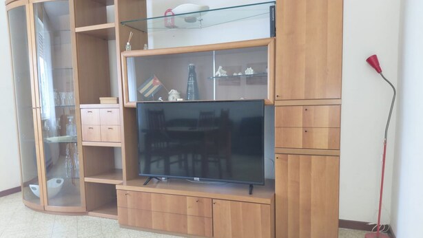 A living room with a wooden entertainment unit, a flat-screen TV, and a glass-fronted cabinet.