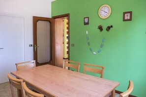 A dining area with a wooden table and chairs, a green wall with a clock, and a partially open door leading to a room with shelves. - A11 - Varano, delightful three-room apartment with garden (Ancona)