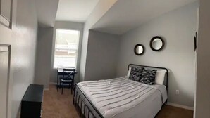 Une chambre à coucher comprenant un lit, un bureau et deux miroirs fixés au mur.