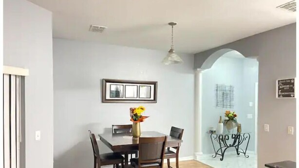 Un coin repas avec une table et des chaises en bois, un vase de fleurs et un luminaire au plafond.