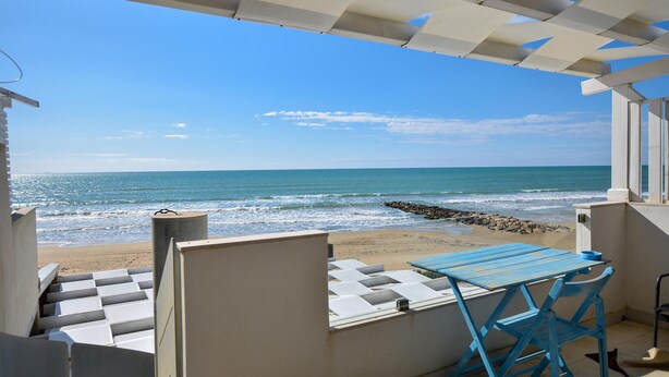 Une vue sur la plage depuis une terrasse couverte, avec une table et des chaises.