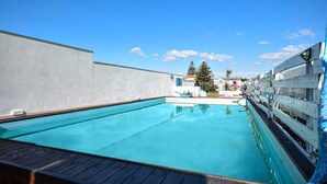 Une piscine dotée d’une terrasse en bois, entourée d’un mur blanc et d’une clôture en bois.