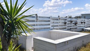 Une terrasse avec une clôture en bois peinte en blanc, une rambarde en métal et un petit espace jardin agrémenté d’un palmier.