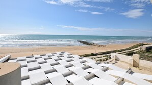 Une plage avec vue sur la mer, des chaises longues blanches et une digue rocheuse.