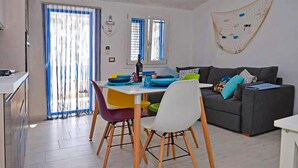 Un salon moderne avec un canapé gris, des fauteuils colorés et une table à manger agrémentée d’assiettes bleues et jaunes.