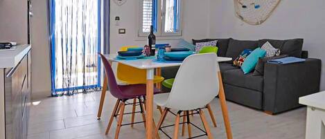 A modern living room with a grey sofa, colorful chairs, and a dining table with blue and yellow plates.