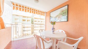 A balcony with a white table and chairs, a vase with flowers, and a painting on the wall.