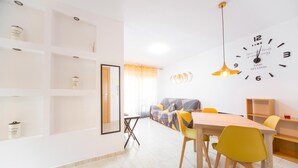A modern living room with a sofa, dining table, chairs, and a wall clock.
