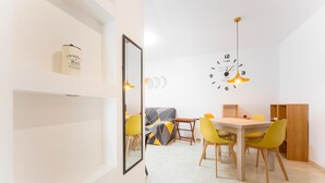 A modern dining area with a wooden table and yellow chairs, a wall clock, and a framed picture of a rice cooker.