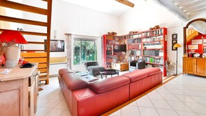 A spacious living room with a red sofa, a bookshelf, and a dining area with a wooden table and chairs. - Stunning home in Eyragues (Eyragues)