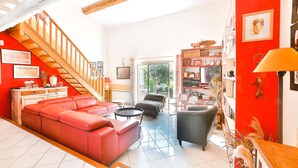 A living room with a red sofa, a black armchair, a wooden staircase, and a bookshelf. - Stunning home in Eyragues (Eyragues)