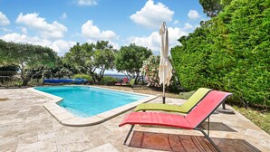 A swimming pool with a tiled deck, surrounded by lush greenery and a clear sky. - Stunning home in Eyragues (Eyragues)