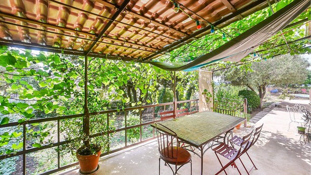 A covered patio with a table and chairs, surrounded by greenery and a view of trees. - Stunning home in Eyragues (Eyragues)