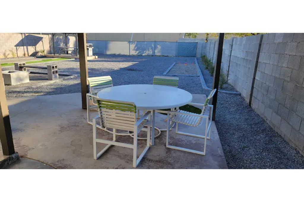 A round table with four chairs, a concrete floor, and a gravel area in the background.