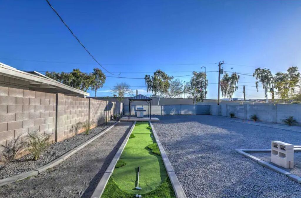 Un patio con césped verde, una piscina pequeña y una zona de juegos de hormigón.