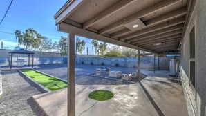 An outdoor patio area with a concrete floor, a green artificial turf section, and a seating arrangement. - Modern-Downtown-PHXairport-Firepit-BBQ-MiniGolf (Phoenix)