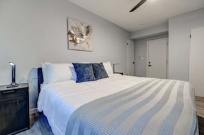Un dormitorio con una cama grande, una mesita de noche, una lámpara de pared y una puerta.