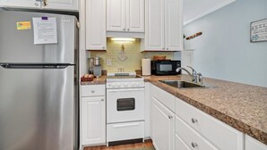 A compact kitchen with white cabinets, stainless steel appliances, a granite countertop, and a backsplash.