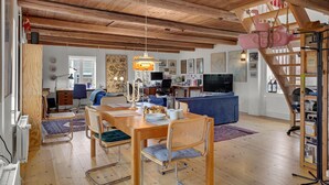 Ein geräumiger Wohnbereich mit Holzboden, einem Esstisch mit Stühlen, einem blauen Sofa und einem Fernseher.