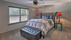 A bedroom with a bed, a ceiling fan, a window with blinds, a nightstand with a lamp, and a bench. - Hogden Home Near the Black Fork River & Trails! (Hodgen)
