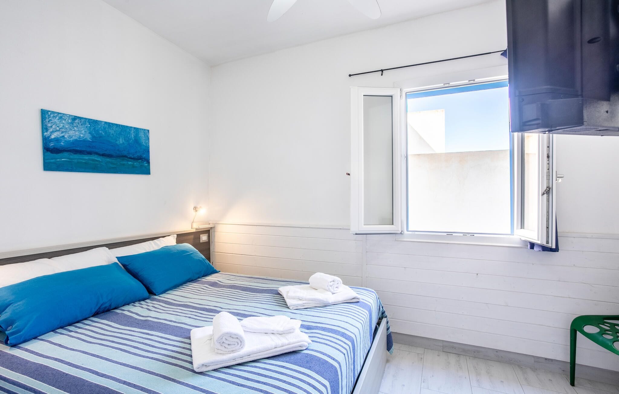Een slaapkamer met een bed, een schilderij, een raam en een groene stoel.