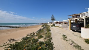 Eine Küstenstraße mit Sandstrand, blauem Himmel und einer Reihe von Häusern mit einem geparkten Auto.