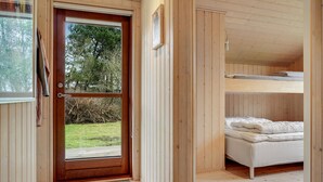 L’intérieur d’un chalet en bois, avec une porte donnant sur un jardin, un lit superposé et un canapé blanc.