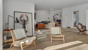 A spacious living room with a large framed lobster print, a wooden chair with a white furry throw, a glass coffee table, and a bookshelf filled with books and decorative items. - Stunning home in Gilleleje with kitchen (Gilleleje)