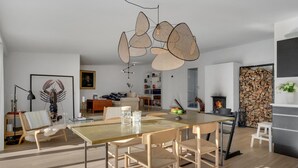 A modern living room with a dining area, featuring a large wooden table, comfortable seating, a fireplace, and a bookshelf. - Stunning home in Gilleleje with kitchen (Gilleleje)