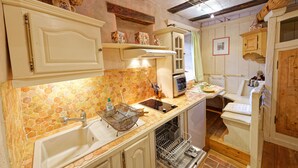 Una cucina compatta con paraschizzi in piastrelle, un lavello, un fornello e un'area pranzo con una sedia.