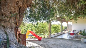 Zona de porxo coberta amb taula i cadires, tobogan i estructura de joc de fusta.
