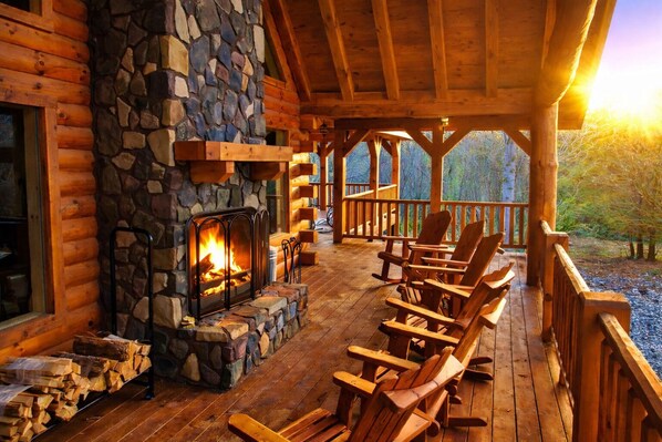 A log cabin with a stone fireplace, wooden deck, and Adirondack chairs.