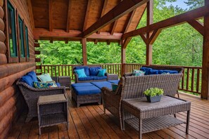 A covered outdoor deck with wicker furniture and a view of a forest.