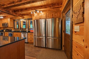 Interior de una cabaña de madera con una cocina que cuenta con un refrigerador de acero inoxidable, armarios de madera y un ventanal grande.