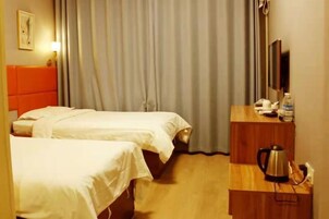 Habitación de hotel con dos camas, un escritorio de madera con hervidor, televisión y cortina.