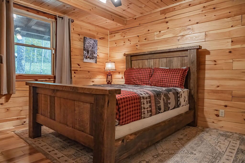 Un dormitorio de cabaña de madera con una cama, una mesita de noche, una lámpara y una ventana.