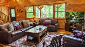 L’intérieur chaleureux d’un chalet avec un canapé en cuir, une table basse et un téléviseur diffusant des images de paysages naturels.