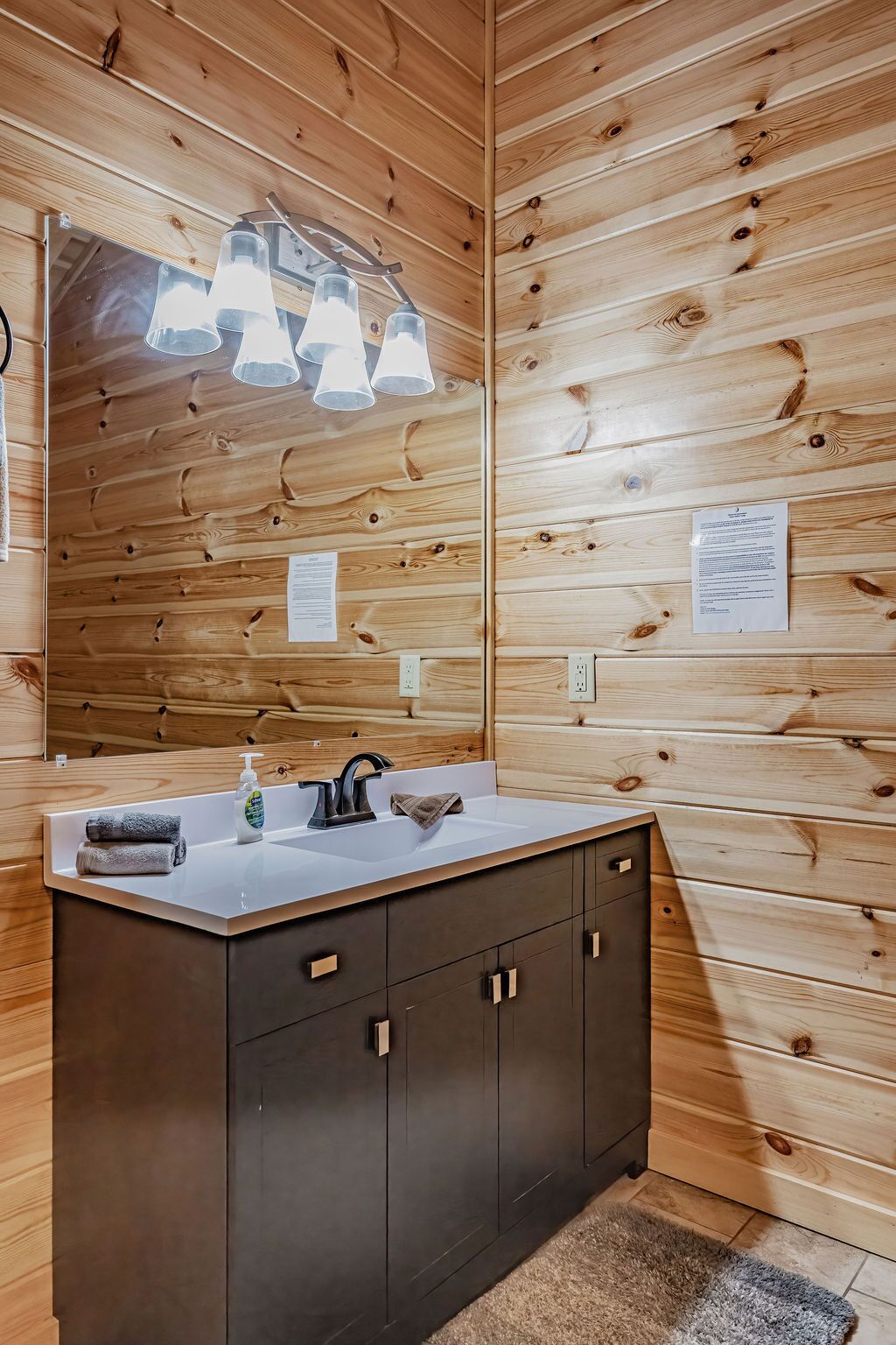 Ein Badezimmer mit Holzwandverkleidung, einem Waschbecken, einem Spiegel und einem Handtuchspender.