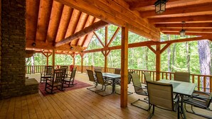 Un espace extérieur abrité, doté de poutres en bois, d’un mur en pierre et d’une table avec des chaises.