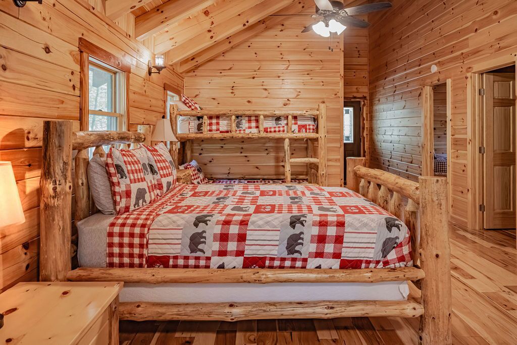 A log cabin bedroom with a bed, a bench, and a ceiling fan.