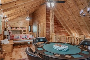 Een gezellig chaletinterieur met een ronde tafel, een bed met geruit beddengoed en een trap naar een hoger niveau.