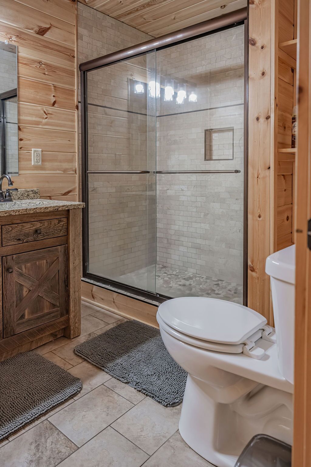 A bathroom with a glass shower enclosure, a white toilet, and a wooden vanity with a sink.