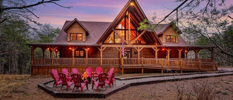 Una cabaña de troncos con una amplia terraza, asientos exteriores y una chimenea.